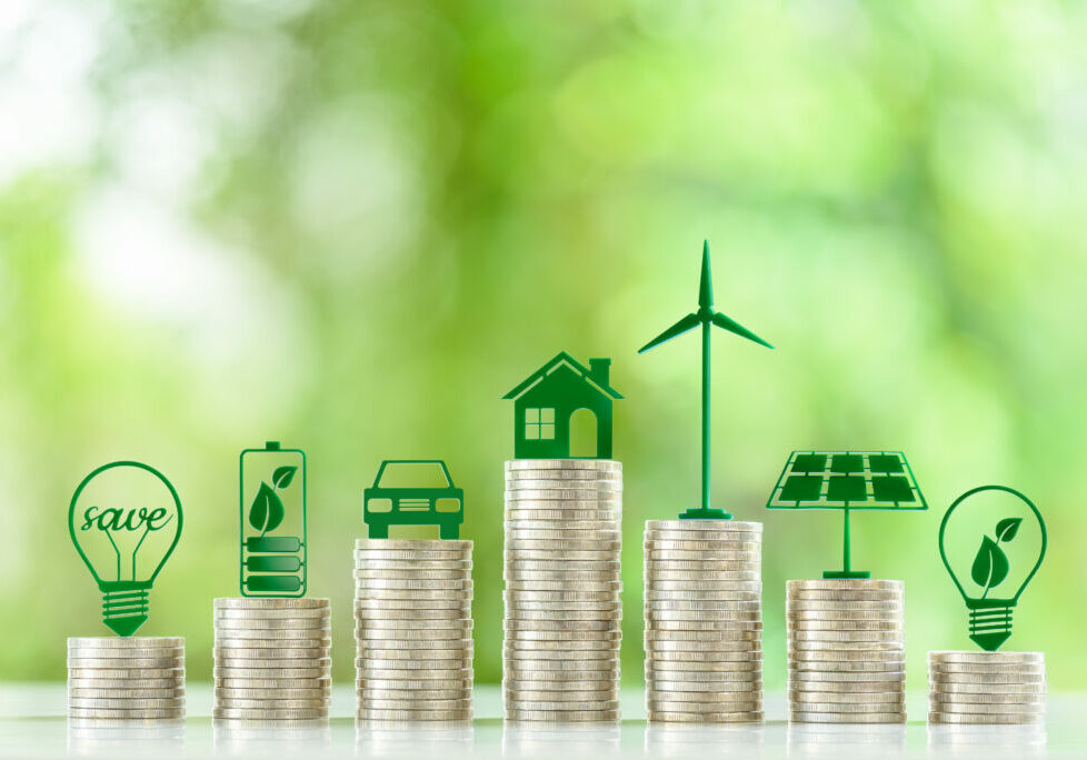 Renewable or clean energy generation prices and costs, financial concept : Green eco-friendly symbols atop coin stacks e.g. energy efficient light bulb, a battery, a solar cell panel, a wind turbine.